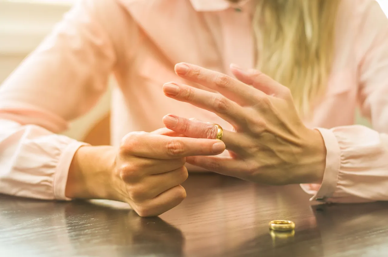 Eine Frau zieht ihren Ehering vom Finger. Der Ring und die Hände sind im Fokus, der Hintergrund ist unscharf.