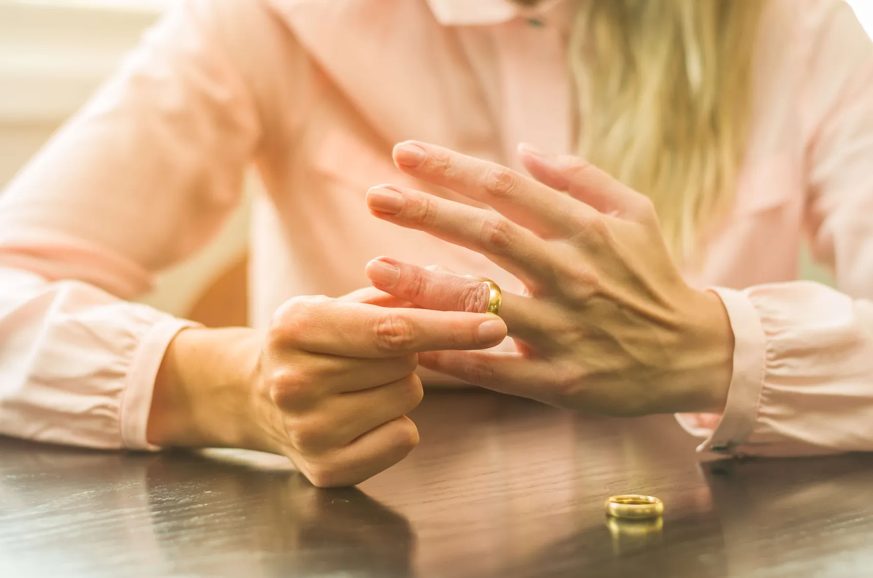 Eine Frau zieht ihren Ehering vom Finger. Der Ring und die Hände sind im Fokus, der Hintergrund ist unscharf.
