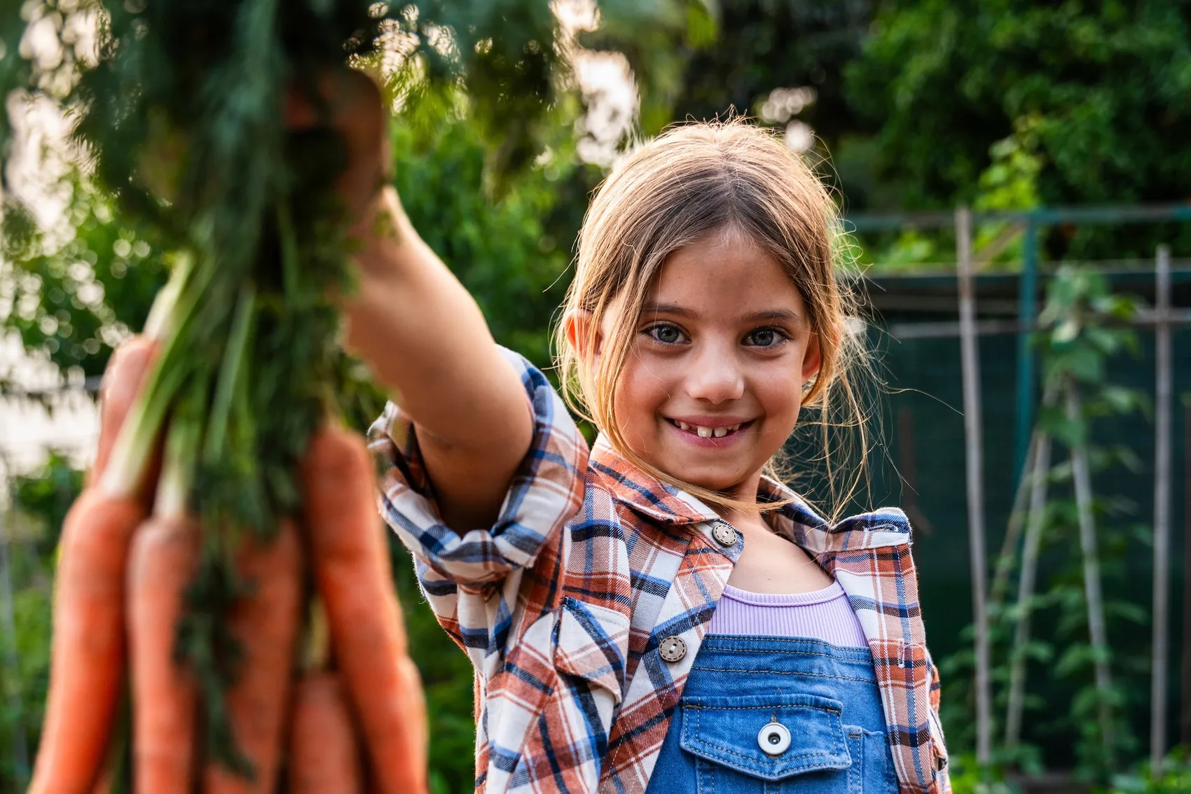 Lächelndes Mädchen hält einen Bund frisch geernteter Karotten in die Höhe.